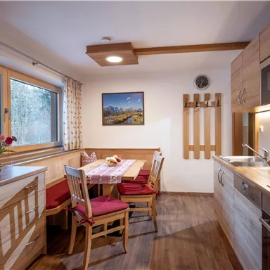Eine moderne Küche mit Holzschränken und einer gemütlichen Sitzecke. Am Tisch stehen frische Blumen und eine schöne Aussicht durch das Fenster.