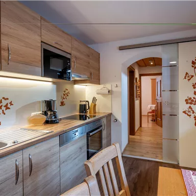 Eine moderne Küche mit Holzschränken und einem eleganten Design. Im Hintergrund ist ein gemütlicher Essbereich zu sehen.