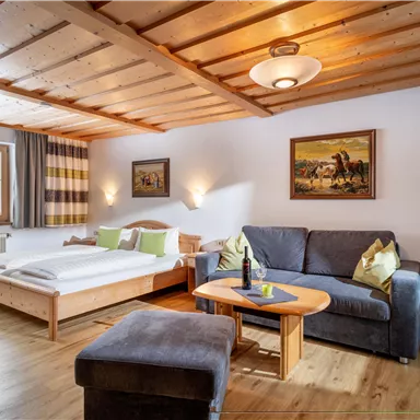 Ein gemütliches Zimmer mit einem Doppelbett und einem Sofa. Die Holzdecke und die warmen Farben schaffen eine einladende Atmosphäre.