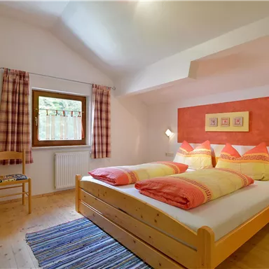 A cozy bedroom with two beds and colorful bedspreads. The walls are painted in soft colors, and there is a window with a view outside.