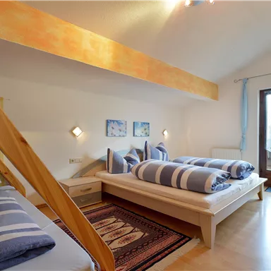 A bright bedroom with two beds and striped bed covers. The room has large windows and a cozy atmosphere.