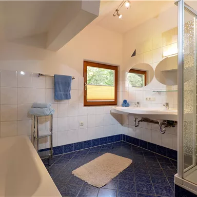 A bright bathroom with a bathtub and a shower. The walls are tiled, and there is a window that lets in natural light.
