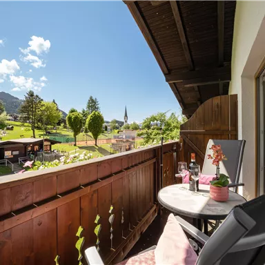 A beautiful balcony overlooking a green landscape and blue sky. On the table are a bottle of wine and a plant.
