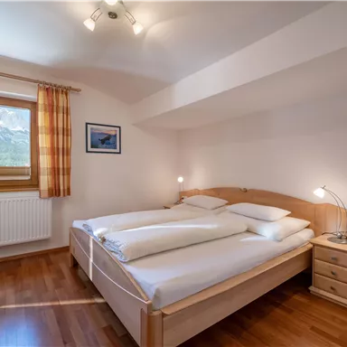 A cozy bedroom with two beds and natural light. There is a nightstand and a pleasant view through the window.