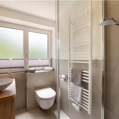 A modern bathroom with a shower and a sink. There are large windows that let in plenty of light.