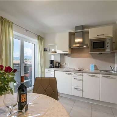 A modern kitchen unit with elegant furnishings. On the table, there is a bottle of wine and a vase with red roses.