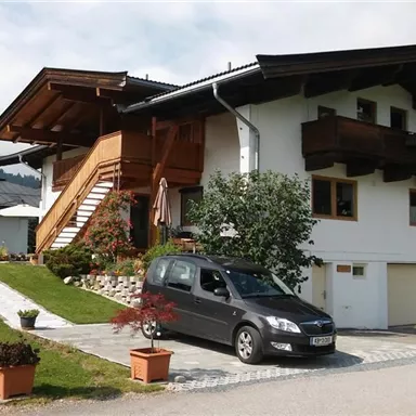 A beautiful house in alpine style with a large garden and a car in front of the driveway. It has a wooden balcony and an inviting staircase.