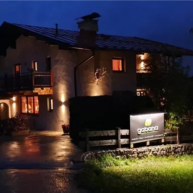 Ein gemütliches Haus bei Nacht, beleuchtet von warmen Lichtern. Im Vordergrund ist ein Schild mit der Aufschrift „gazana“ sichtbar.