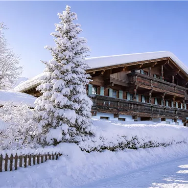 A beautiful chalet in winter with a snow-covered roof and trees. The clear blue sky gives the scene a peaceful atmosphere.