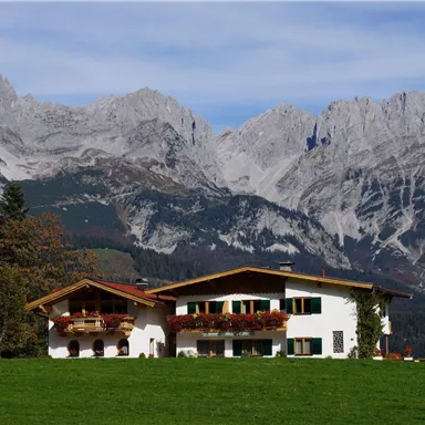 Ein schönes Haus in den Alpen, umgeben von grünen Wiesen und beeindruckenden Bergen. Der Himmel ist klar und die Natur strahlt Ruhe aus.