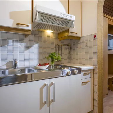 Eine moderne Küchenecke mit einem Waschbecken, Herd und einer Mikrowelle. Die Wände sind mit hellen Fliesen gefliest und die Beleuchtung sorgt für eine freundliche Atmosphäre.