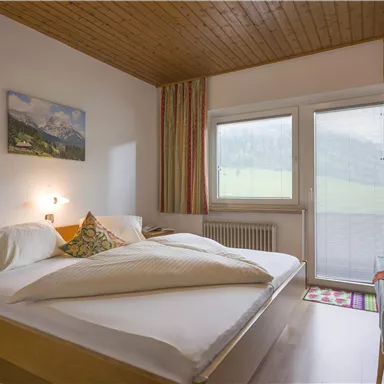 Ein gemütliches Schlafzimmer mit einem Doppelbett und hellen Wänden. Große Fenster bieten einen Blick auf die umliegende Landschaft.
