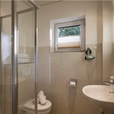 Ein modernes Badezimmer mit einer Dusche und einem Waschbecken. Helle Wände und ein Fenster sorgen für eine freundliche Atmosphäre.