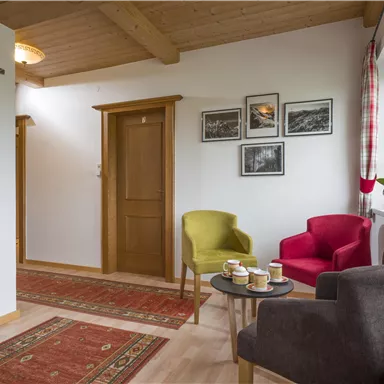 Ein einladender Flur mit bunten Sesseln und einem kleinen Tisch. An der Wand hängen Bilder, und ein Teppich verleiht dem Raum Gemütlichkeit.