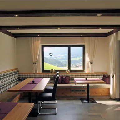 Ein modernes Restaurant mit Holztischen und bunten Kissen. Große Fenster bieten einen Blick auf die umliegenden Berge.