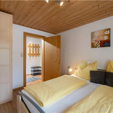 Ein gemütliches Schlafzimmer mit einem Doppelbett und gelben Bettbezügen. Der Raum hat Holzdecken und eine offene Tür, die zu einem weiteren Bereich führt.