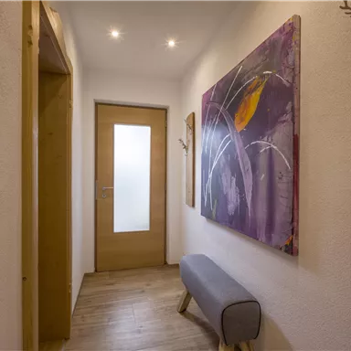A bright hallway with wooden panels and a large, colorful mural. The entrance door is made of wood and has a glass element.