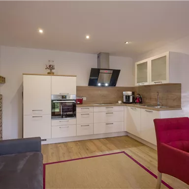 A modern kitchen with bright cabinets and an elegant cooking area. The room is friendly and inviting, with a cozy sofa and red chairs.