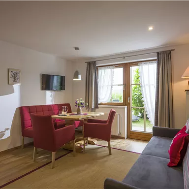 A cozy living room with a dining area and a sofa. Large windows let in plenty of light and offer a view of the outdoors.