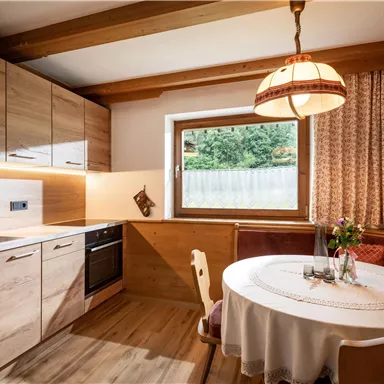 Eine moderne Küche mit Holzmöbeln und einem runden Tisch. Durch das Fenster fällt natürliches Licht und es gibt eine gemütliche Atmosphäre.