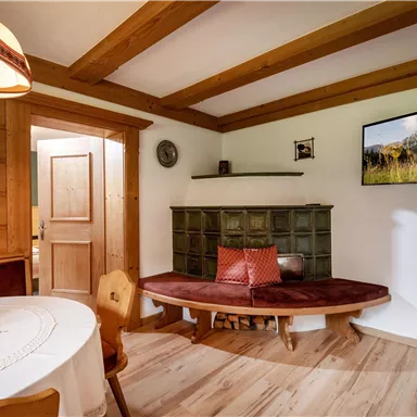 Ein gemütlicher Raum mit Holzverkleidung und einem runden Tisch. An der Wand hängt ein Bild von einer Berglandschaft, und eine Sitzbank lädt zum Entspannen ein.