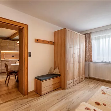 Ein gemütliches Zimmer mit Holzschränken und einem großen Fenster. Der Boden ist aus Holz, und im Hintergrund sieht man einen Essbereich.