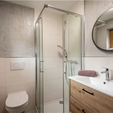 Ein modernes Badezimmer mit einer Dusche und einem Waschbecken. Handtücher und ein Fenster mit Blick ins Freie ergänzen den Raum.