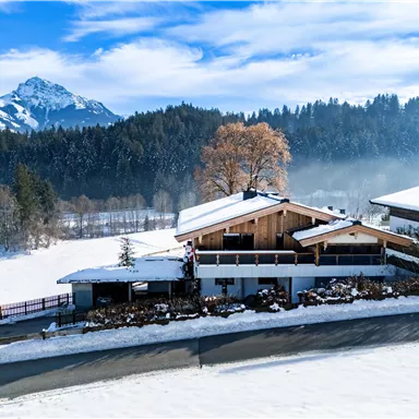 A beautiful winter house surrounded by snow-covered fields and mountains. The sky is clear and the snow sparkles in the sun.