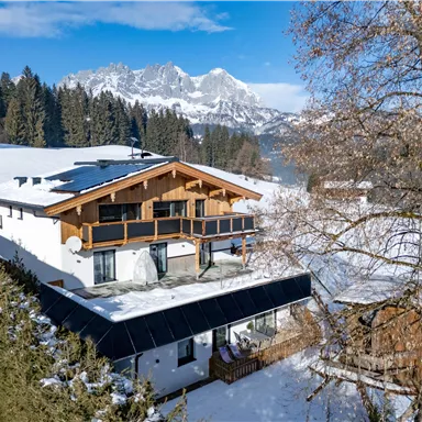 A charming farmhouse in the Alps, surrounded by snow-covered mountains. The blue sky and sunny landscape create an idyllic winter atmosphere.