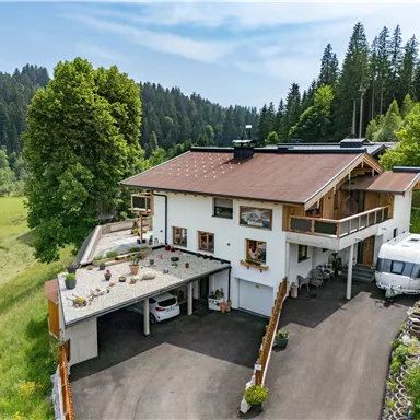 Ein modernes Haus umgeben von viel Grün und Bäumen. Es gibt einen gepflegten Garten und einen Parkplatz neben dem Gebäude.