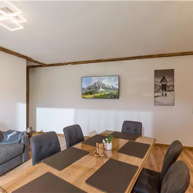 Ein modernes Esszimmer mit einem großen Holztisch und schwarzen Stühlen. An der Wand hängen Bilder von Landschaften.