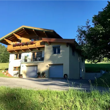A modern house with wooden decorations and a large entrance area. Surrounded by meadows and trees, it radiates a calm atmosphere.