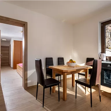 Eine helle und moderne Küche mit einem Esstisch und Stühlen. Im Hintergrund ist ein Fenster mit Ausblick auf eine ruhige Landschaft.