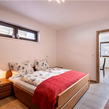 Ein helles Schlafzimmer mit einem Doppelbett und hübscher Bettwäsche. Es gibt einen Holzschrank und ein Fenster mit Tageslicht.