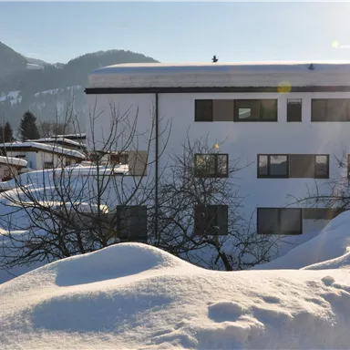Eine verschneite Landschaft mit einem modernen Gebäude im Vordergrund. Im Hintergrund sind sanfte Hügel und ein klarer Himmel zu sehen.