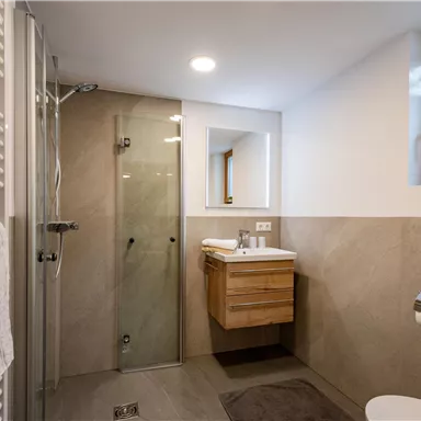 Ein modernes Badezimmer mit einer Glasdusche und einem Holzwaschtisch. Helle Wände und ein Fenster sorgen für eine angenehme Atmosphäre.