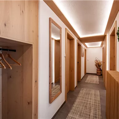 Ein moderner Flur mit Holzverkleidung und einer hellen Beleuchtung. An der Wand hängen Spiegel und eine Dekoration aus Pflanzen.