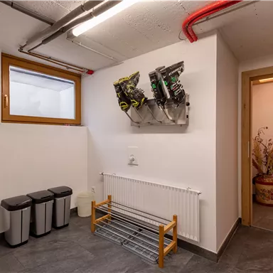 Ein moderner Eingangsbereich mit einem Garderobenständer und Müllbehältern. An der Wand hängen verschiedene Gegenstände, und eine Tür führt zu einem weiteren Raum.