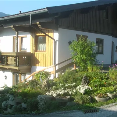 A cozy house in traditional style with wooden cladding and colorful flower boxes. The well-maintained garden completes the picture.
