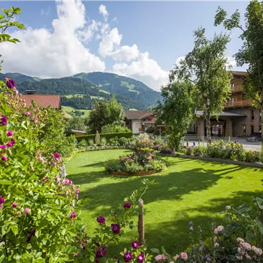 Ein schöner Garten mit bunten Blumen und grünem Rasen. Im Hintergrund sind Berge und eine klare blaue Himmelslandschaft zu sehen.