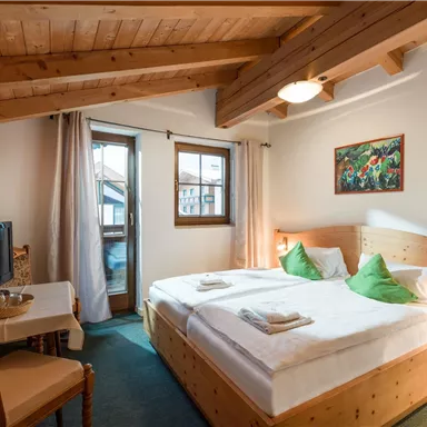 Ein gemütliches Schlafzimmer mit einem Doppelbett, frischen Kissen und Holzdecke. Es gibt einen Tisch und einen Fernseher sowie ein Fenster mit Blick nach draußen.