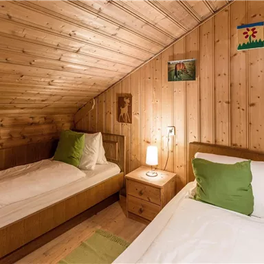 Ein gemütliches Schlafzimmer mit zwei Einzelbetten und Holzvertäfelungen. Eine kleine Nachttischlampe und einige Bilder sorgen für eine einladende Atmosphäre.