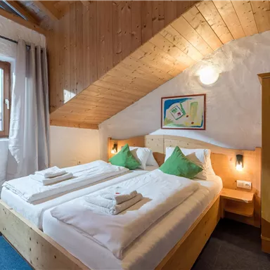 Ein gemütliches Schlafzimmer mit zwei Betten und grünen Kissen. Holzvertäfelung und ein Fenster sorgen für eine einladende Atmosphäre.