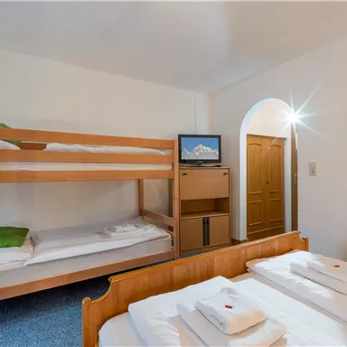 Ein einfaches Zimmer mit einem Etagenbett und einem Doppelbett. Der Raum ist hell und freundlich eingerichtet.