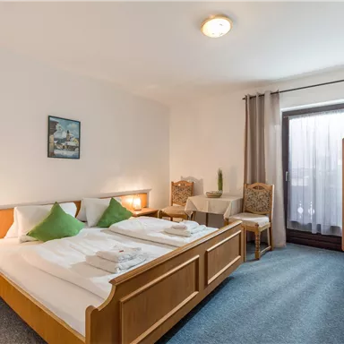 Ein helles Zimmer mit einem Doppelbett und einem Etagenbett. Es gibt Stühle und einen Zugang zu einem Balkon.