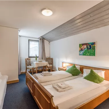 Ein gemütliches Hotelzimmer mit zwei Betten und hellen Möbeln. Es gibt einen kleinen Tisch mit Stühlen und einen Fernseher an der Wand.