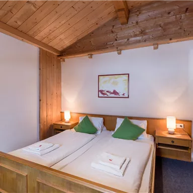 Ein gemütliches Schlafzimmer mit Holzdecke und zwei Einzelbetten. Der Raum ist hell und freundlich mit Nachttischen und Tischlampen.