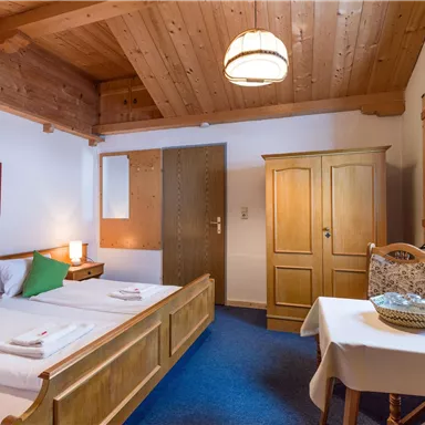 Ein gemütliches Zimmer mit zwei Betten und Holzdetails. Ein Tisch und eine Kommode sind ebenfalls vorhanden, dazu ein Fenster mit natürlichem Licht.