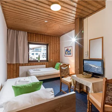 Ein gemütliches Zimmer mit Holzvertäfelung, einem Fenster und zwei Betten. Es gibt einen Tisch, Stühle und einen Fernseher.