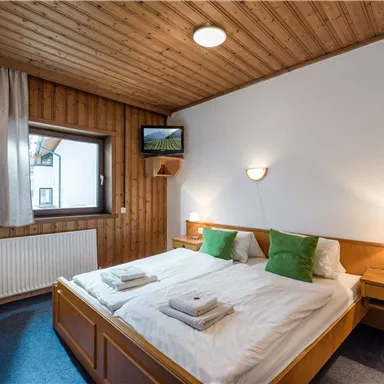 Ein gemütliches Schlafzimmer mit zwei Einzelbetten und hellen Kissen. Holzverkleidung und ein Fenster sorgen für eine einladende Atmosphäre.